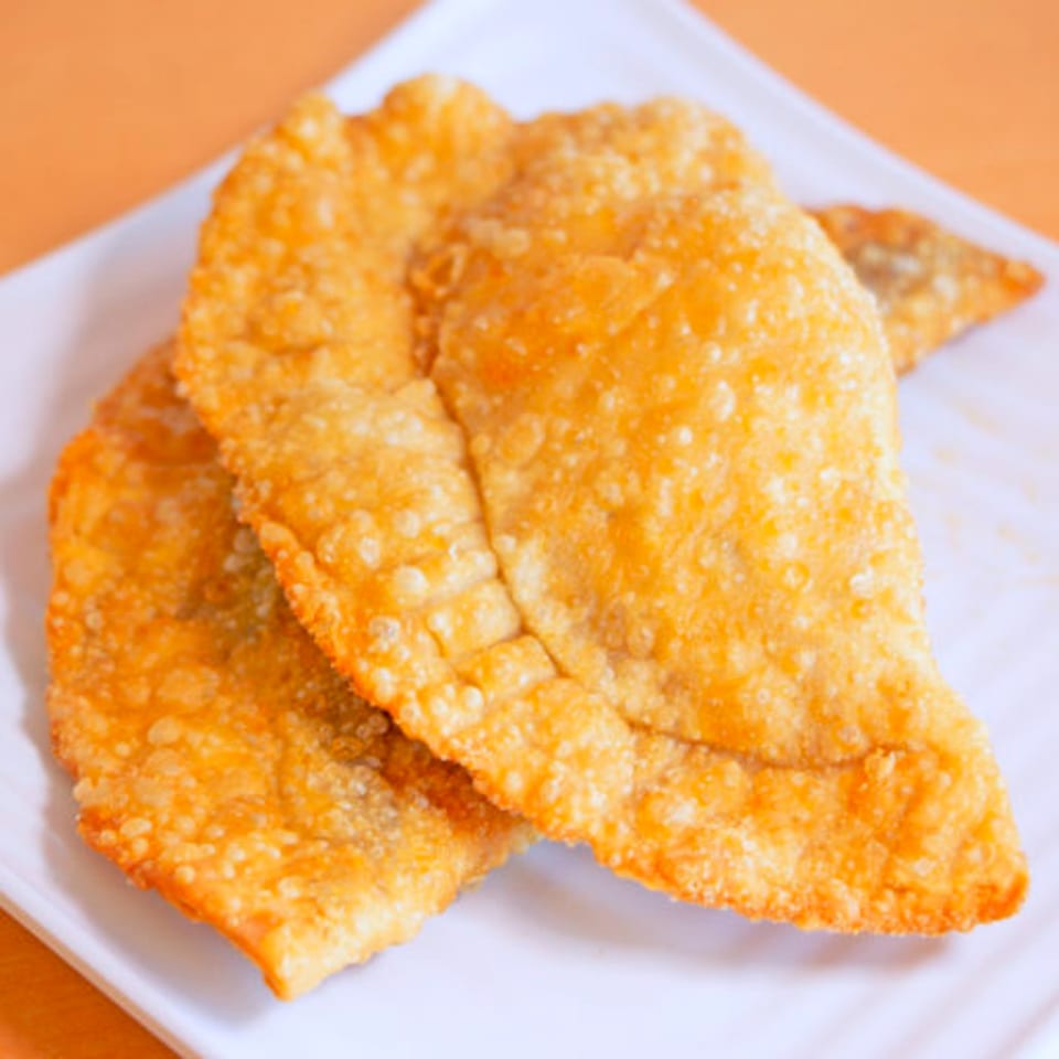 Two golden-brown, crispy Dominican empanadas, or pastelitos, on a white plate.