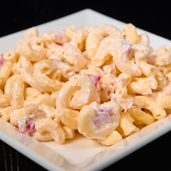 Close-up of creamy macaroni salad with small red and purple pieces in a white square dish.