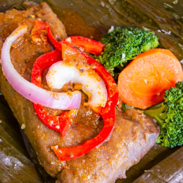 Dominican pasteles, a meat-filled masa dish, garnished with red peppers, onions, broccoli, and carrots.