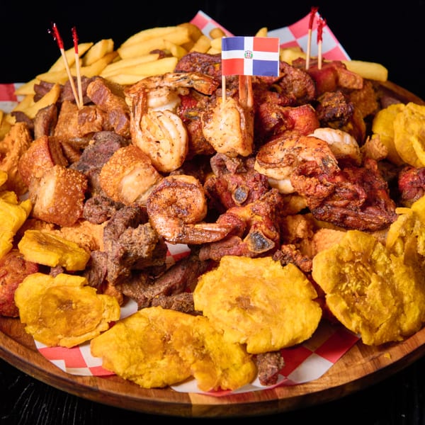 A large platter of Dominican fried meats, shrimp, plantains, and fries with a Dominican flag pick.