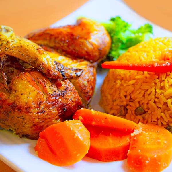 Roasted chicken with yellow rice, red pepper, and sweet potatoes on a white plate.
