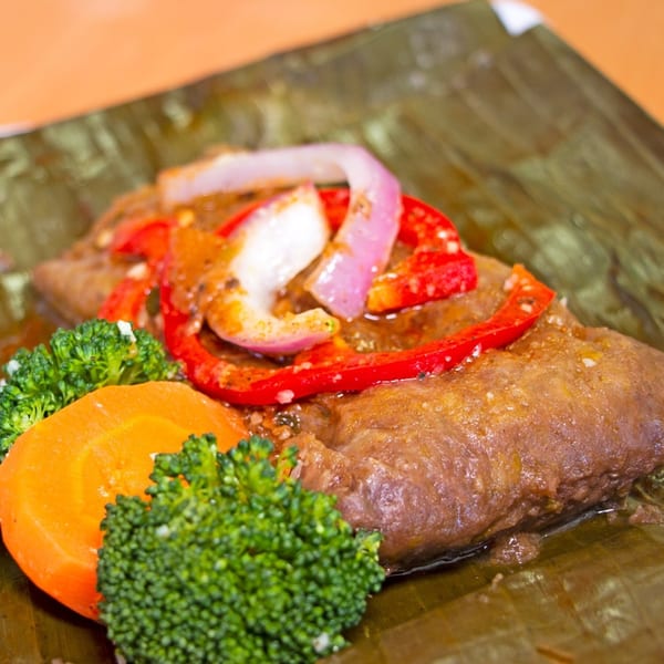 Dominican pasteles en hoja with red peppers, onions, broccoli, and carrots, served on a banana leaf.