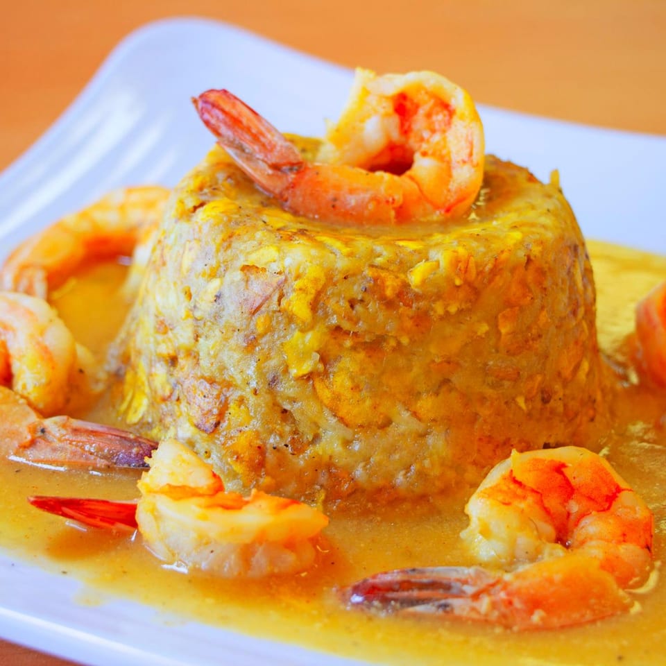 Mofongo with shrimp in a yellow sauce, served on a white rectangular plate.