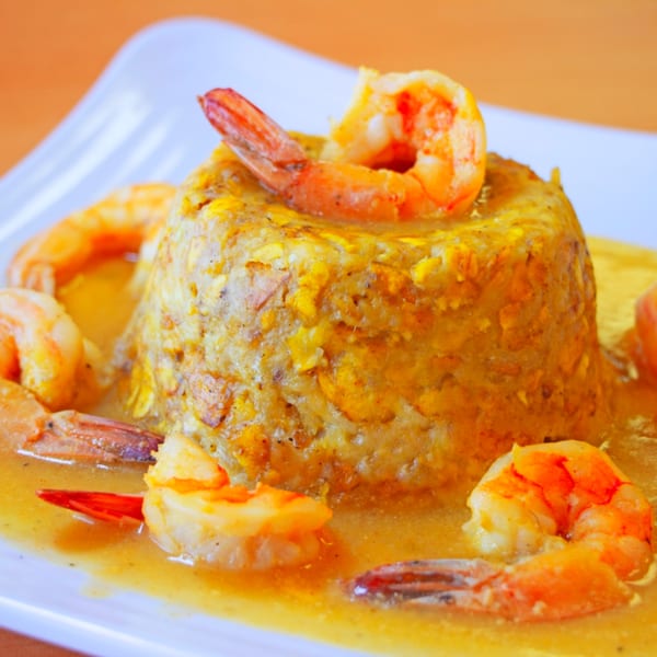 Mofongo with shrimp, a traditional Dominican dish, served in a rich yellow sauce on a white plate.