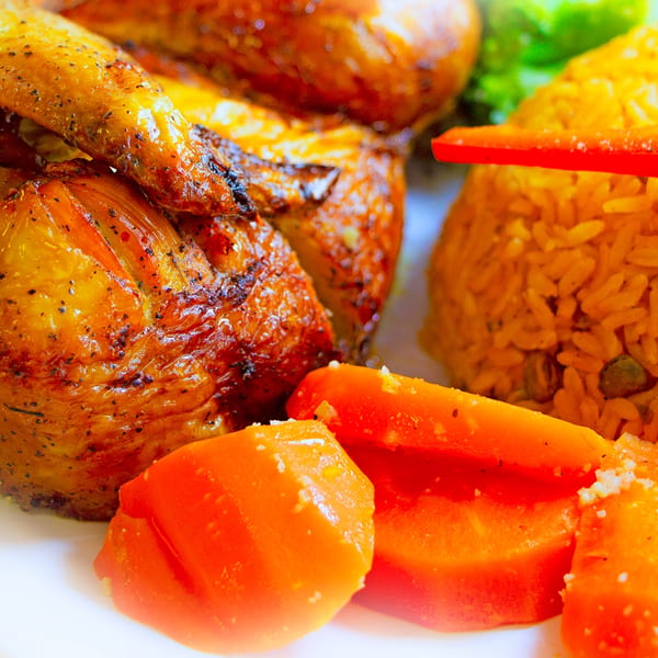 Close-up of roasted chicken, yellow rice, and orange vegetables on a white plate.
