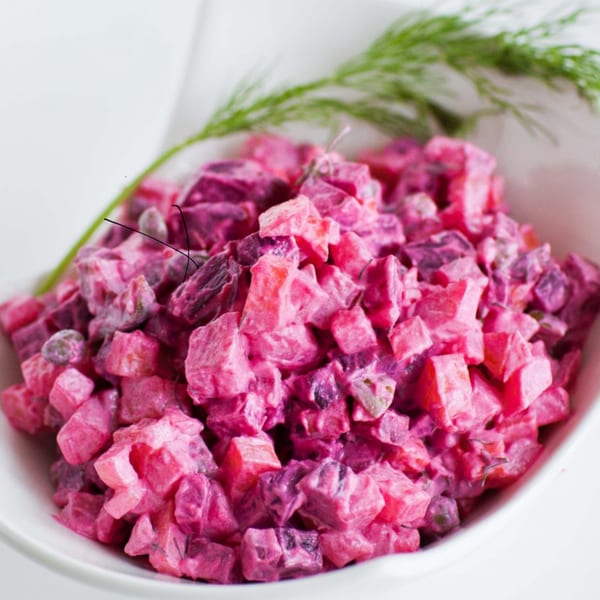 Close-up of a vibrant pink salad with diced vegetables and a sprig of dill in a white bowl.