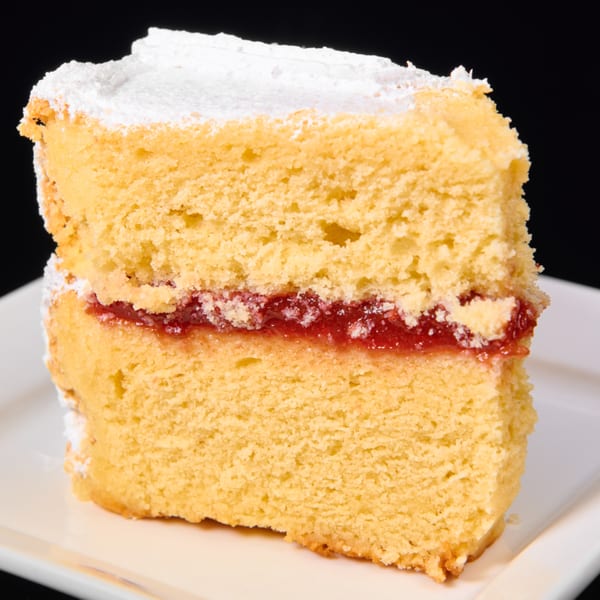 A slice of yellow cake with a strawberry jam filling and powdered sugar on top.