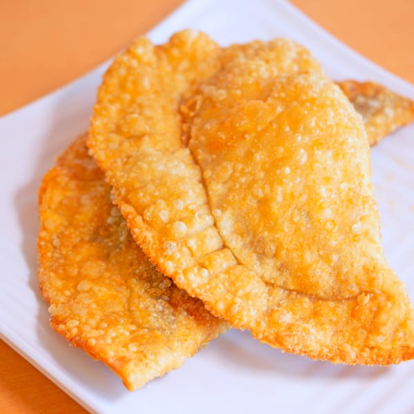 Two golden-brown, crispy Dominican empanadas on a white plate, against an orange background.