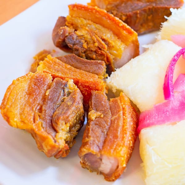 Crispy fried pork belly (chicharron) with yucca and pickled red onions on a white plate.